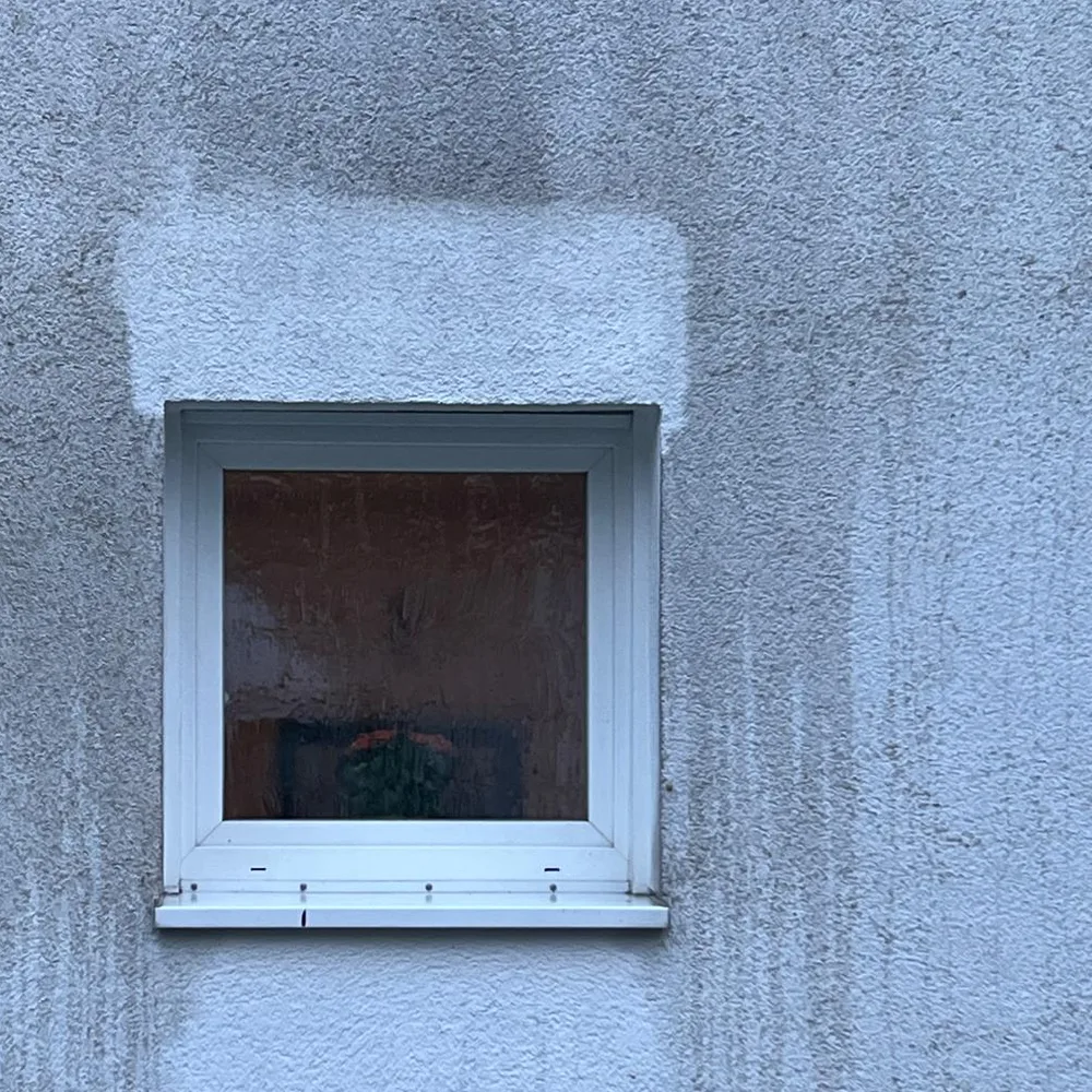 Probefläche über einem Fenster: der gereinigte Streifen ist hell, die Wand daneben noch grau